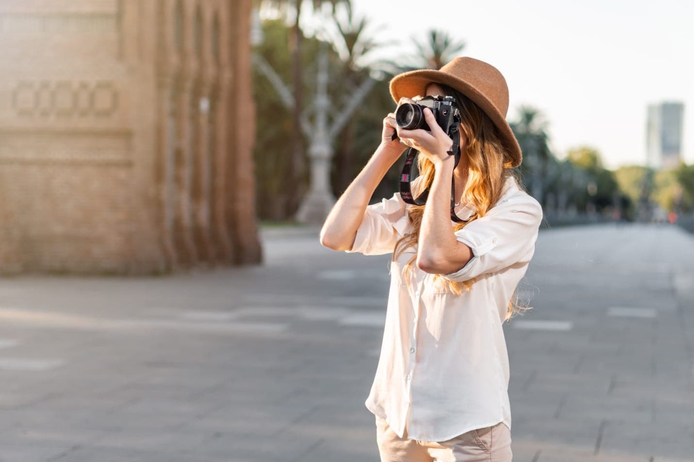 Una fotógrafa con cámara y sombrero de ala ancha fotografía una calle de Barcelona al atardecer